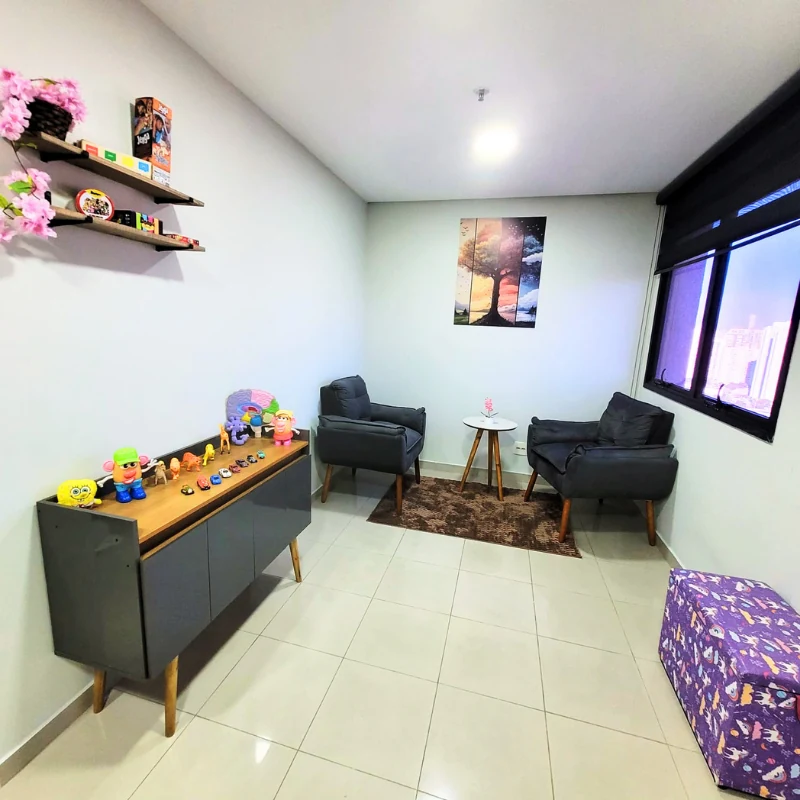 Sala de atendimento, com poltronas, mesa de apoio e materiais lúdicos de avaliação