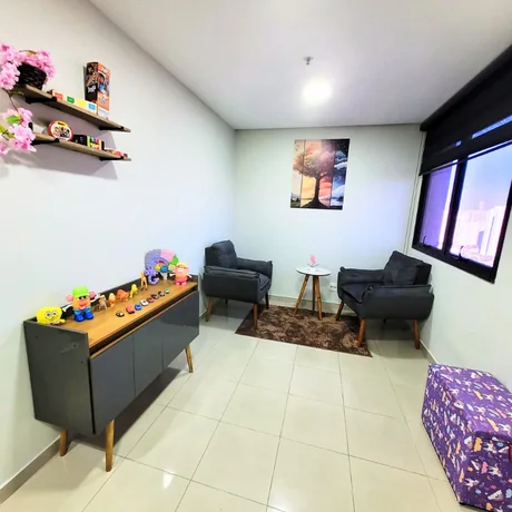 Sala de atendimento, com poltronas, mesa de apoio e materiais lúdicos de avaliação